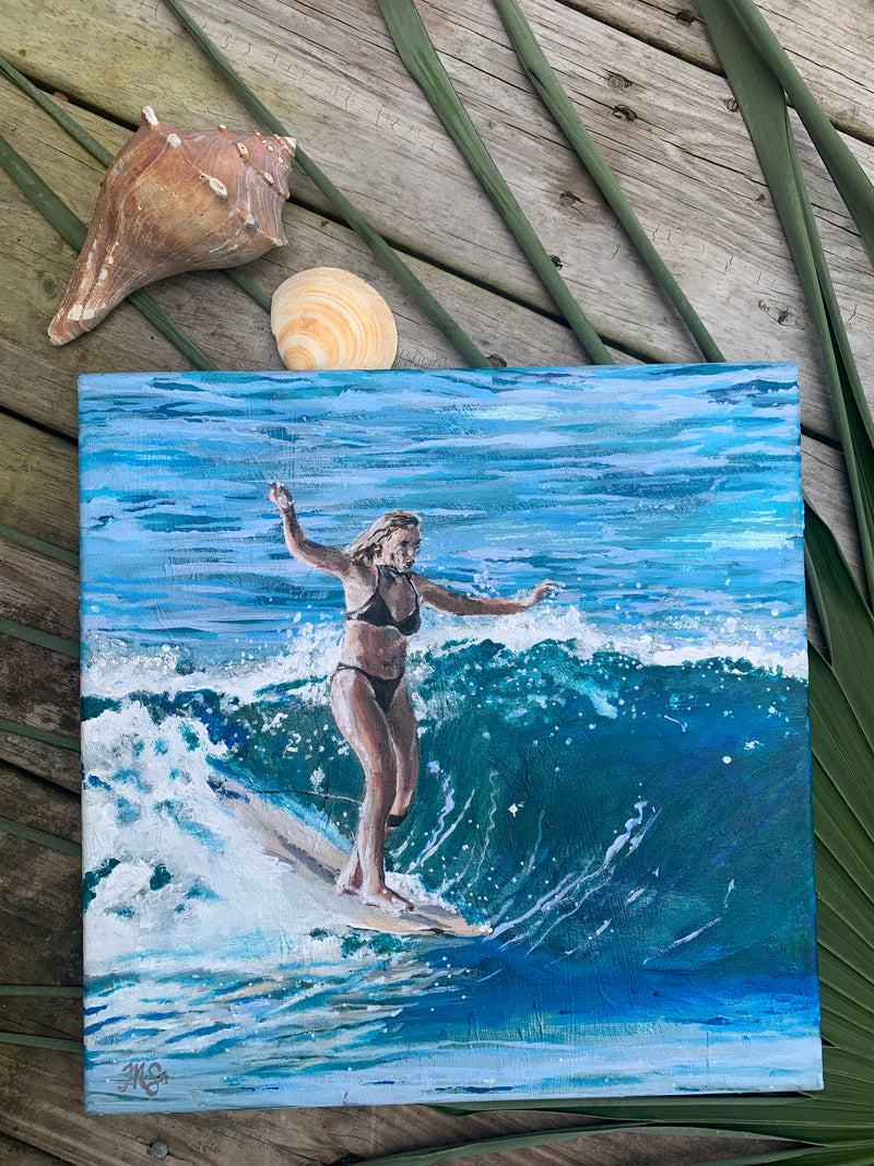 Painting of a woman surfing on a wave with shells and leaves on a wooden surface