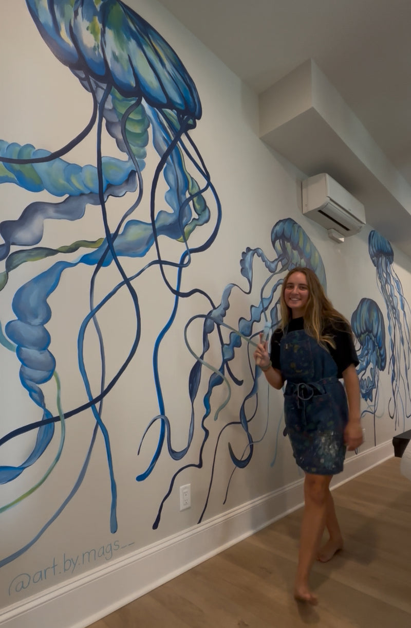 North Carolina Artist standing in front of a wall mural of jellyfish in an indoor setting.